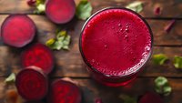 Fresh beetroot juice in glass with raw beets on wooden background. Healthy detox drink rich in vitamins and antioxidants for wellness lifestyle.
