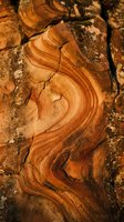 Weathered sandstone rock formation with flowing curved layers and natural erosion patterns creating abstract geological texture in warm earth tones.