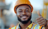 Cheerful African American construction worker in orange hard hat and safety vest showing thumbs up gesture with confident smile at building site.