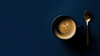 Overhead view of hot espresso coffee in dark mug with golden spoon on deep blue background, suitable for cafe, restaurant, and beverage marketing materials.