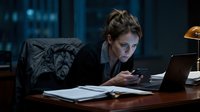 Focused businesswoman reviewing documents and using laptop at desk in modern office environment during late night work session.