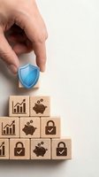 Hand placing blue shield icon on wooden blocks with financial security symbols for business protection and risk management concepts.
