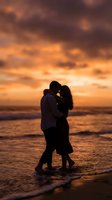 Romantic couple silhouette embracing on beach at sunset with dramatic orange sky and ocean waves creating intimate moment for love and relationship concepts.