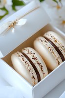 White macarons with chocolate filling and gold sprinkles in elegant gift box with satin ribbon, soft focus background with floral elements. Perfect for wedding favors.