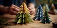 Colorful origami Christmas trees on wooden table with person crafting in background, festive holiday decoration craft project.