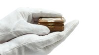Hands wearing white cotton gloves holding small brass decorative box on white background, suitable for antique, luxury, and heritage product photography.