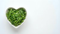 Fresh green arugula leaves in white heart-shaped bowl on clean background for healthy eating and cooking concepts.