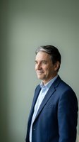 Middle-aged man with gray hair wearing navy blazer and light blue shirt, professional headshot against neutral background for corporate portraits and business profiles.