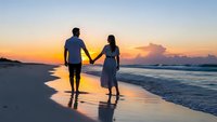 Romantic couple walking hand in hand on beach at sunset with golden sky and ocean waves creating peaceful moment for love and relationship concepts.