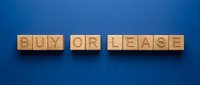 Wooden blocks spelling buy or lease on blue background, representing real estate decision making and property investment choices.