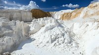 Limestone quarry with white chalk cliffs and mineral deposits under blue sky with fluffy clouds, industrial mining landscape showing raw material extraction.