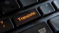 Illuminated translate button on black computer keyboard with orange backlight glowing in dark environment, close-up view showing modern technology interface.
