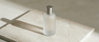 Frosted glass bottle with silver metallic cap on beige stone surface with natural shadows, suitable for cosmetics, skincare, perfume, and beauty product packaging mockups.