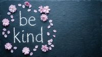 Be kind handwritten text on dark slate surrounded by delicate pink cherry blossom flowers and petals, inspiring kindness and positivity.