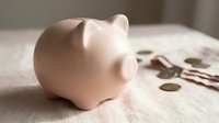 Pink ceramic piggy bank lying on side with scattered coins on wooden surface representing savings and financial planning concepts.