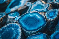 Vibrant blue agate crystal slices with concentric patterns and natural formations showing detailed mineral layers and raw stone edges in macro photography.