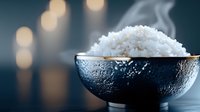 Steaming bowl of cooked white rice with condensation on dark ceramic bowl against blurred bokeh background, suitable for food, cooking, and culinary content.