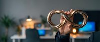 Businessman holding infinity symbol made of copper wire in modern office environment with blurred background and warm lighting.