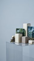 Geometric stone and marble cubes arranged on glass surface with dried botanicals, showcasing luxury materials and modern minimalist design for product display and interior styling.