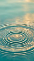 Serene water ripples create concentric circles on calm turquoise surface with soft golden light reflections and peaceful sky backdrop for meditation concepts.