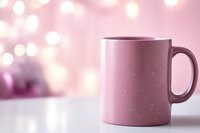 Pink ceramic mug on white surface against soft bokeh background with glowing lights. Minimalist composition with copy space for product mockup or holiday design.