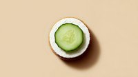 Fresh cucumber slice on coconut half against beige background for spa wellness skincare natural beauty treatment concepts.
