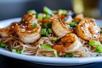 Grilled shrimp with rice noodles garnished with fresh green onions in Asian sauce, served on white plate. Close up view of seafood dish with selective focus.