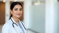 Professional female doctor with stethoscope smiling confidently in modern medical facility wearing white coat for healthcare and medicine concepts.