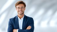 Confident young Caucasian businessman in navy suit and glasses smiling with crossed arms in modern office corridor for corporate marketing materials.