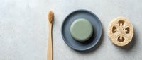 Zero waste bathroom essentials with bamboo toothbrush, natural soap bar and loofah sponge arranged on marble surface for eco-friendly lifestyle.