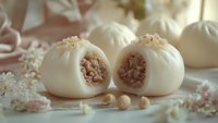 Steamed pork buns with meat filling cut in half, displaying tender dough and savory interior, surrounded by scattered pearls and additional buns on neutral surface for food styling and culinary content.