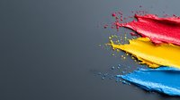 Vibrant paint splashes in primary colors of red, yellow and blue against dark background create dynamic motion effect with flying droplets and liquid texture.