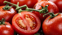 Fresh ripe red tomatoes with green stems, one cut in half showing seeds and flesh. Organic vegetables for healthy cooking and salads.