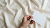 Hand holding blank white card on beige fabric background for business branding, stationery mockup, and marketing presentations.