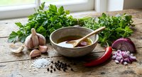 Fresh herbs and spices arranged on rustic wooden table with ceramic bowl and wooden spoon for cooking preparation and culinary seasoning.