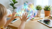 Young blonde child interacting with colorful holographic sphere displaying futuristic technology interface at wooden desk with plants and tablet.