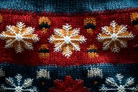 Festive winter knitted pattern with white snowflakes on red and blue stripes background, close up view of traditional holiday sweater texture.