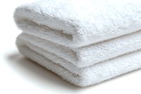 Clean white folded cotton bath towels stacked neatly on white background, showing soft texture and layers for spa, hotel and bathroom concepts.