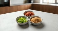 Three ceramic bowls with colorful spices and herbs on white marble countertop in modern kitchen for cooking and culinary preparation.