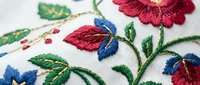Colorful floral embroidery with red flowers, blue butterflies and green leaves on white fabric. Traditional needlework craft for home decor projects.