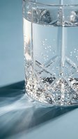 Crystal cut glass tumbler filled with sparkling water on blue surface with soft natural lighting and elegant shadows for luxury beverage photography.