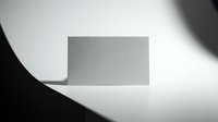 Blank gray business card on white surface with dramatic shadow lighting, ready for branding and corporate design projects.