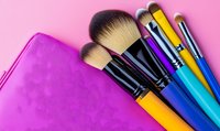 Colorful professional makeup brushes with soft bristles and bright handles arranged on pink background with cosmetic bag for beauty and fashion concepts.