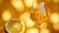 Elegant wine glass filled with golden white wine next to fresh lemon slice against warm bokeh background, perfect for beverage, hospitality and lifestyle marketing.
