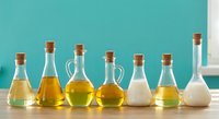 Various cooking oils and liquids in glass bottles with cork stoppers arranged on wooden surface against turquoise wall in kitchen.