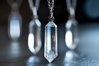 Clear quartz crystal pendant on silver chain with blurred crystals in background, spiritual healing jewelry for meditation and energy work.