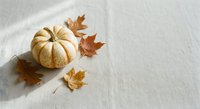 Small decorative pumpkin with autumn maple leaves on neutral linen fabric background for seasonal fall harvest thanksgiving home decor crafts.