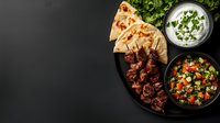 Grilled lamb kebabs served with flatbread, fresh herb yogurt sauce and traditional Middle Eastern salad on dark background. Perfect for restaurant menu photography.