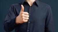 Businessman in navy blue shirt showing thumbs up gesture against dark background, conveying approval and positive feedback in professional setting.