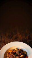 Braised meat with root vegetables in rich sauce served in white bowl on dark wooden surface, overhead view with copy space for culinary, restaurant, and food styling applications.